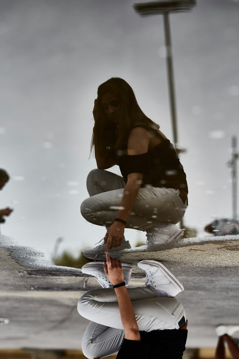 woman in black off-shoulder shirt with gray denim jeans pointing on the water with her reflection during daytime