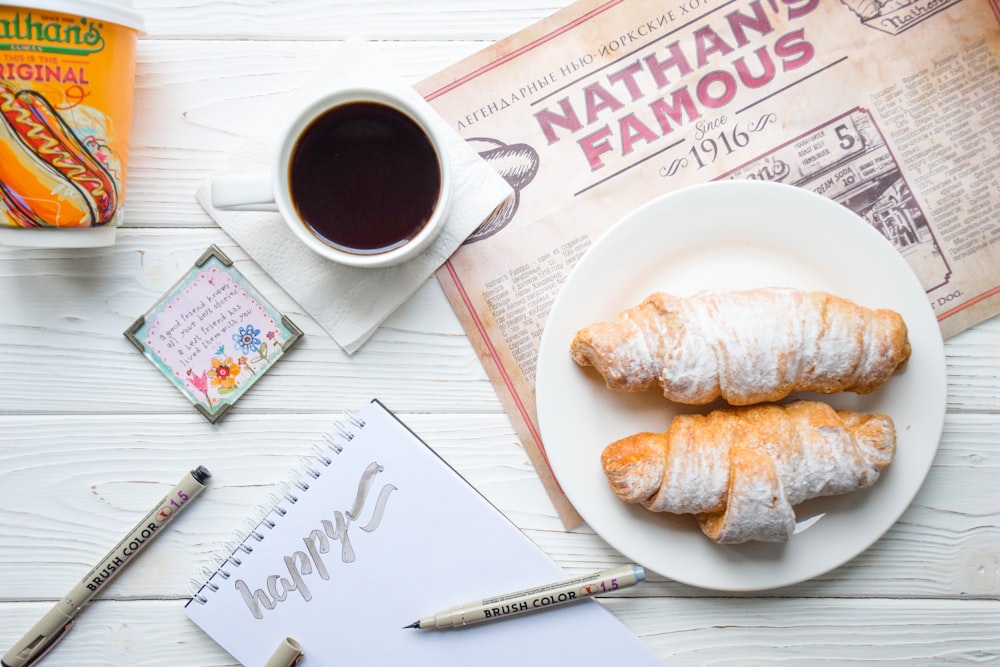flat lay photography of croissant bread on plate beside mug filled with brown liquid