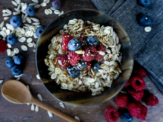 A rustic wooden bowl filled with steaming oat porridge topped with fresh berries and nuts on a cozy kitchen table.