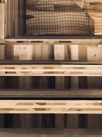 Wooden steps with a natural finish, and a netting above. The stairs have simple, clean lines and are constructed from planks of wood, showcasing different grains and shades. There are metal bolts visible on the sides, providing structural support.