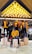Mannequins dressed in coordinated fashion outfits, predominantly in shades of yellow and black, are displayed on wooden platforms in a well-lit store. The ceiling features an array of hanging light bulbs that add to the contemporary ambiance.
