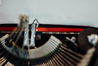 A close-up view of a vintage typewriter. Some typewriter keys and the typed words 'hi MINLac s testing' are visible on a piece of paper. The typewriter's metal mechanisms and rulers are prominently displayed.