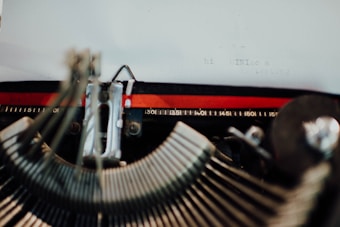 A close-up view of a vintage typewriter. Some typewriter keys and the typed words 'hi MINLac s testing' are visible on a piece of paper. The typewriter's metal mechanisms and rulers are prominently displayed.