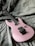A pink electric guitar is placed on a greyish textured fabric background. The guitar features a sleek design with a black bridge and pickups.