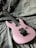 A pink electric guitar is placed on a greyish textured fabric background. The guitar features a sleek design with a black bridge and pickups.