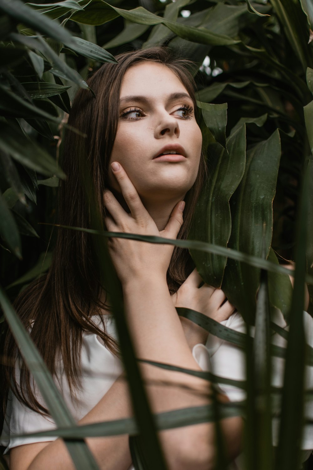 close-up photo of woman holding her neck while standing near plants during daytime