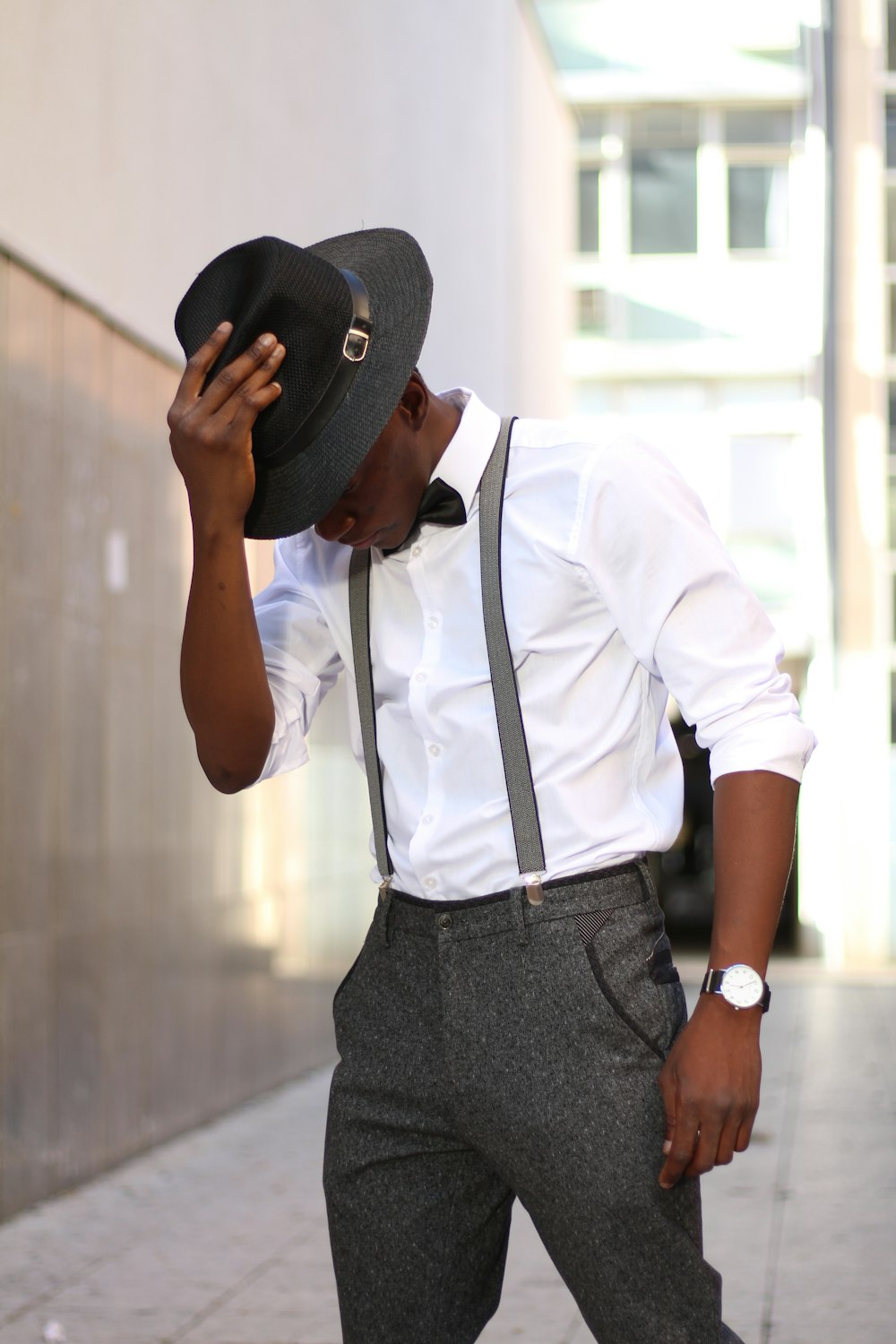 man wearing white dress shirt and gray dress pants holding hat