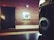 A vintage Lubitel 2 camera is prominently displayed in the foreground on a dark surface. The background features a wooden wall with a chalkboard filled with handwritten script and a square artwork with abstract design that says 'ART' in the center.