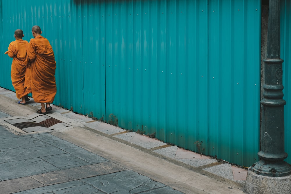 two monks walking beside blue painted galvanized wall