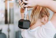 woman holding dumbbell in white crew-neck t-shirt