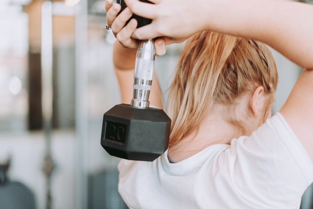 woman holding dumbbell in white crew-neck t-shirt