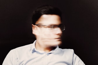 man wearing white button-up collared top and black framed eyeglasses moving head back and forth