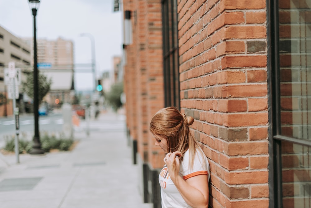 Femme appuyée sur un mur de briques brunes pendant la journée