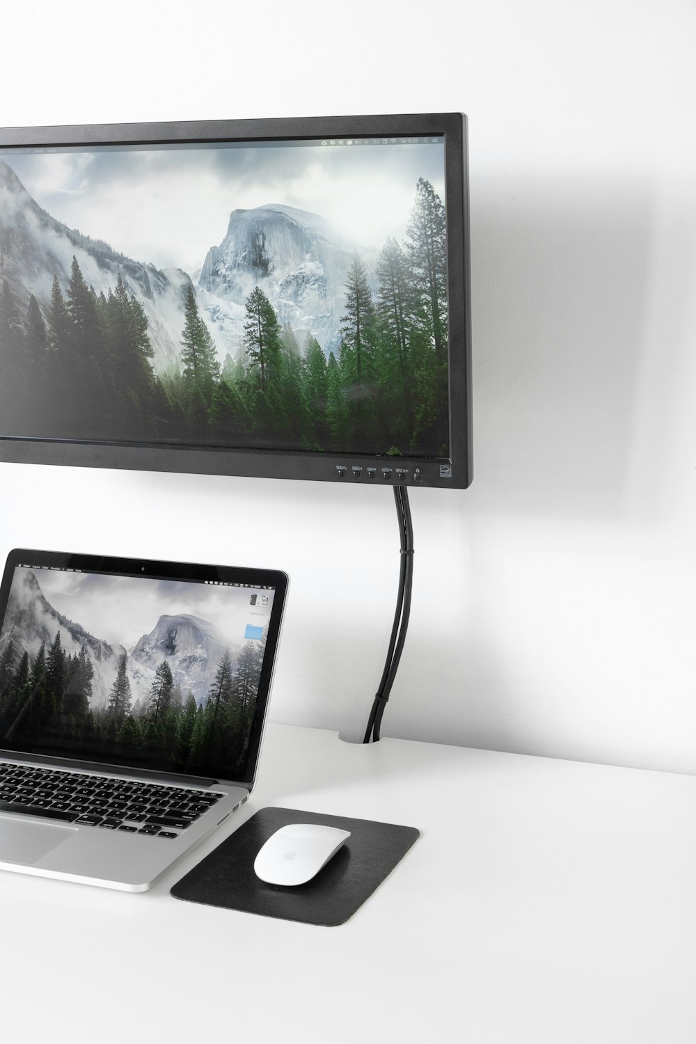 MacBook Pro bajo un monitor de computadora de pantalla plana negra