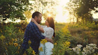 An intimate moment of a couple embracing in a sunlit field with soft sand tones in the background.