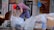 An elderly person wearing a red cap and striped clothing is sorting through several large transparent bags filled with recyclables and cardboard boxes on a city sidewalk. Surrounding the person are signs in another language, some depicting services offered inside nearby establishments.