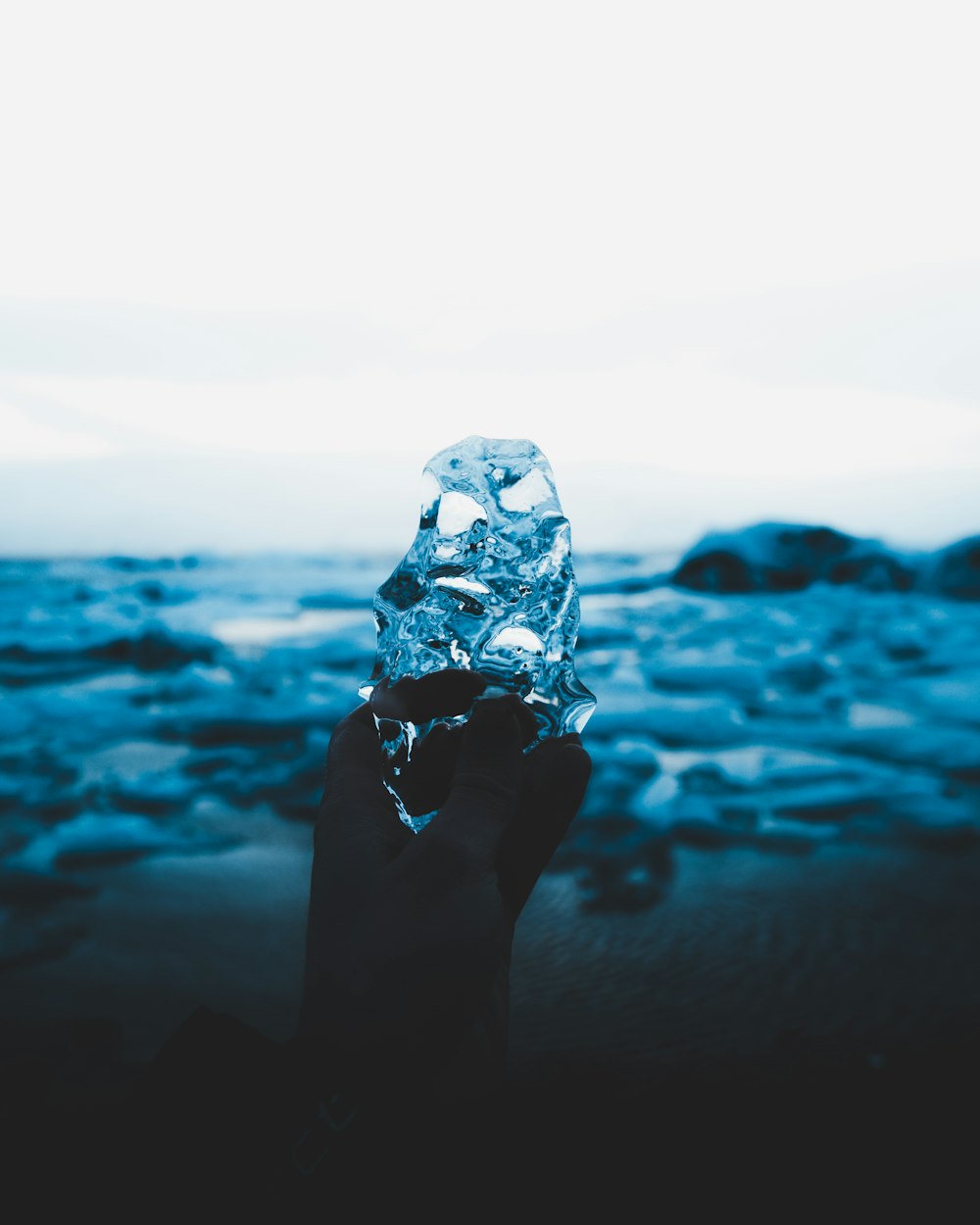 a hand holding an ice block in front of a body of water