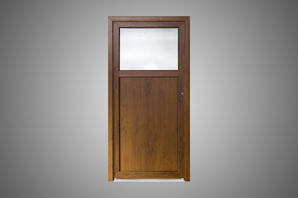 A wooden door with a simple design, featuring a large, frosted glass pane on the upper section and a solid wood panel below. The wood is of a dark brown color with a visible grain pattern. The background is a plain gray, highlighting the door.