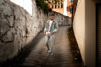A woman walking down an urban alley wearing a cropped leather biker jacket and black skinny jeans, with sunlight casting shadows.