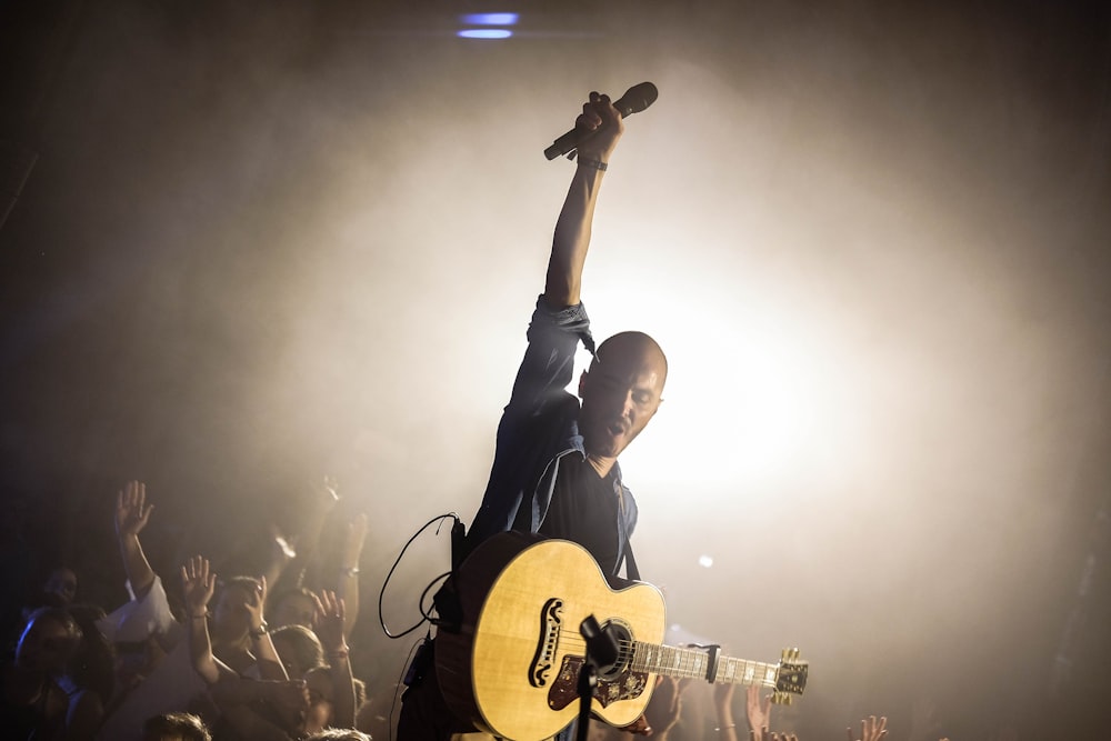 man holding guitar and microphone performing on stage