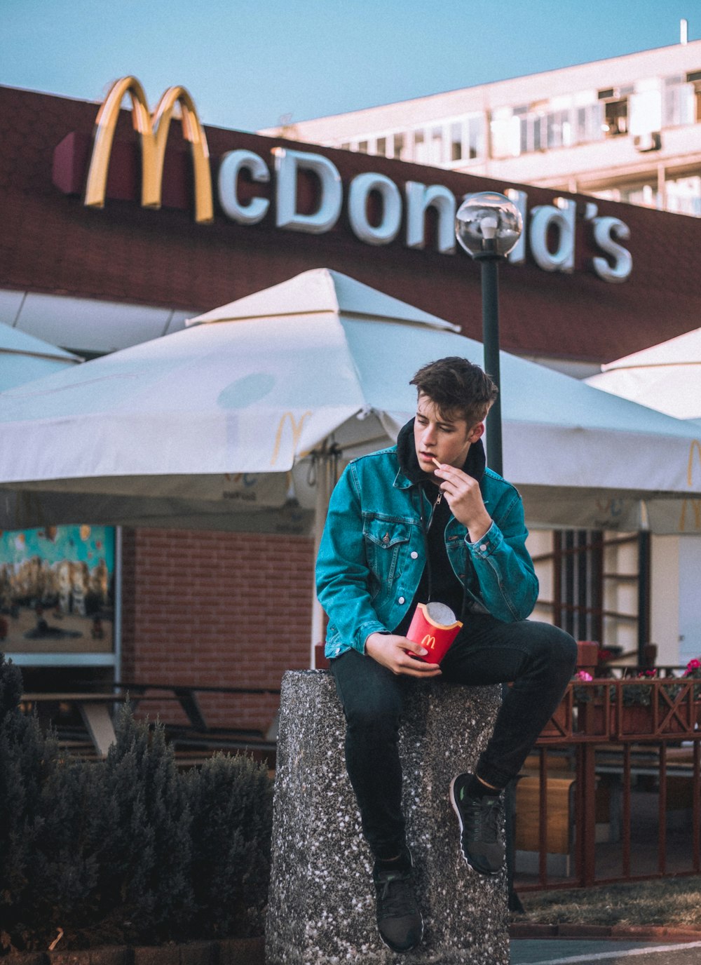person sitting on pillar while eating fried fries outside McDonald's during