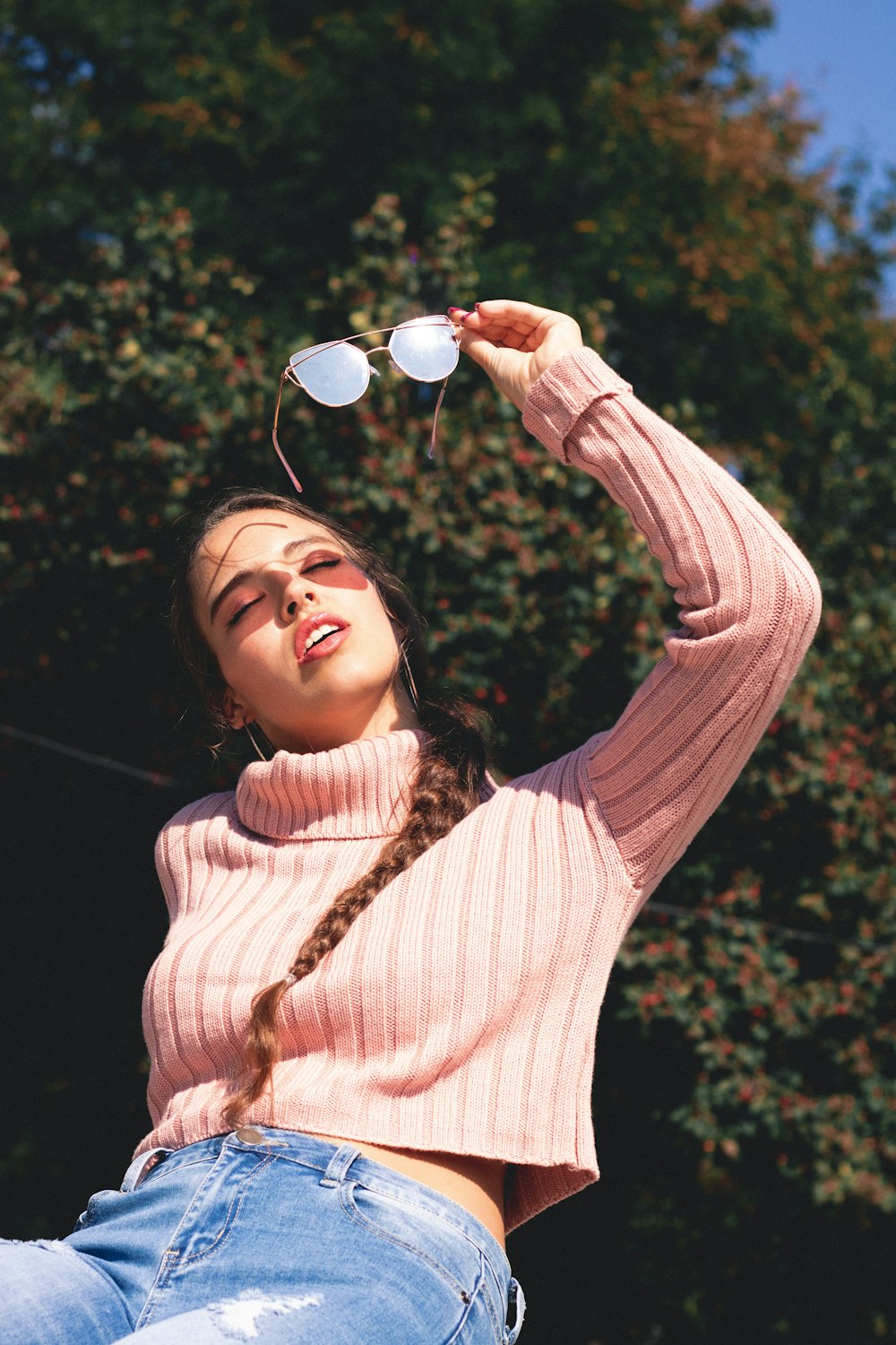 donna che indossa un maglione rosa mentre tiene occhiali da sole