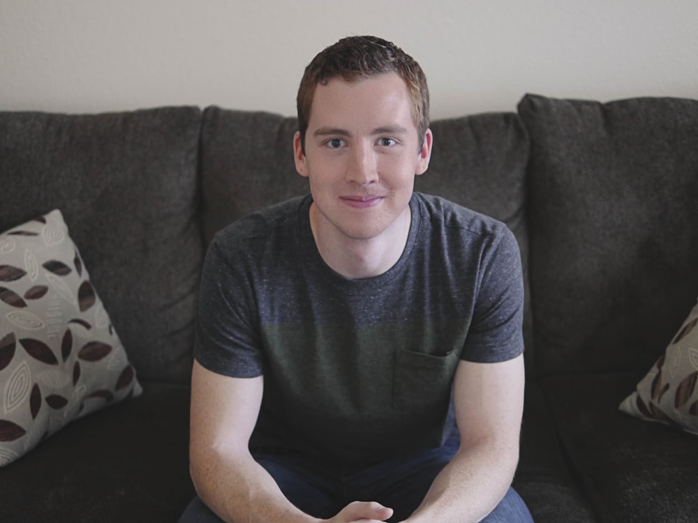 smiling man in gray shirt sitting on sofa