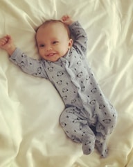 A smiling baby wearing soft cotton clothes sitting on a cozy blanket.