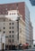 A multi-story building with a retro-style facade houses Hotel San Carlos. The architecture features a large vertical sign with ‘Hotel’ at the top and ‘San Carlos’ running downward. Several flags, including Mexican and Italian, are displayed along the street level. The building is complemented by adjacent modern high-rise buildings.