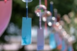 Several colorful paper tags are hanging from strings, possibly as part of a decorative display. The background is blurred, creating a bokeh effect with bright circular lights. A blue tag with a silhouette of a bird is prominently visible in the foreground.