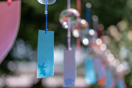 Several colorful paper tags are hanging from strings, possibly as part of a decorative display. The background is blurred, creating a bokeh effect with bright circular lights. A blue tag with a silhouette of a bird is prominently visible in the foreground.