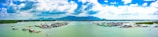 A wide expanse of water with floating structures, possibly fishing farms or houses. There are lush green hills in the background under a partly cloudy sky, creating a serene and expansive landscape.