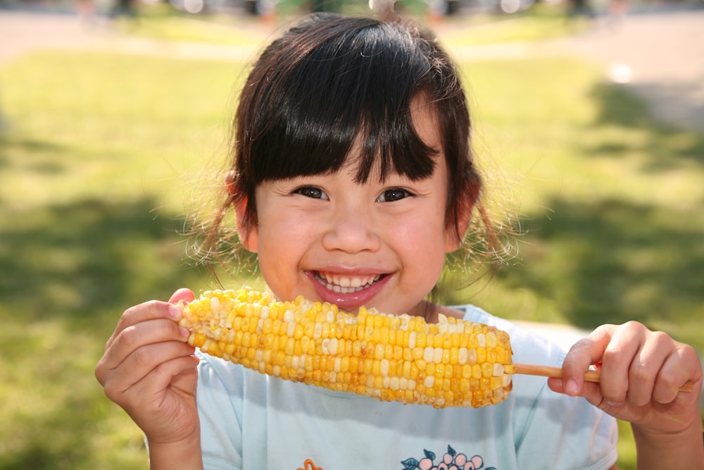 Muchacha sonriente sosteniendo maíz cocido durante el día