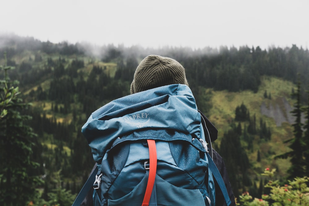 personne portant un sac à dos turquoise regardant la montagne