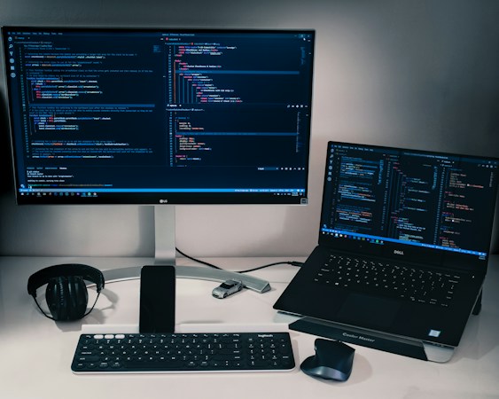 A developer's desk with two monitors of code and an open laptop