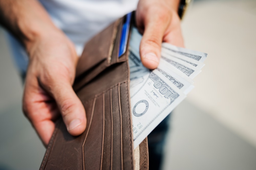 person showing brown leather wallet with banknotes