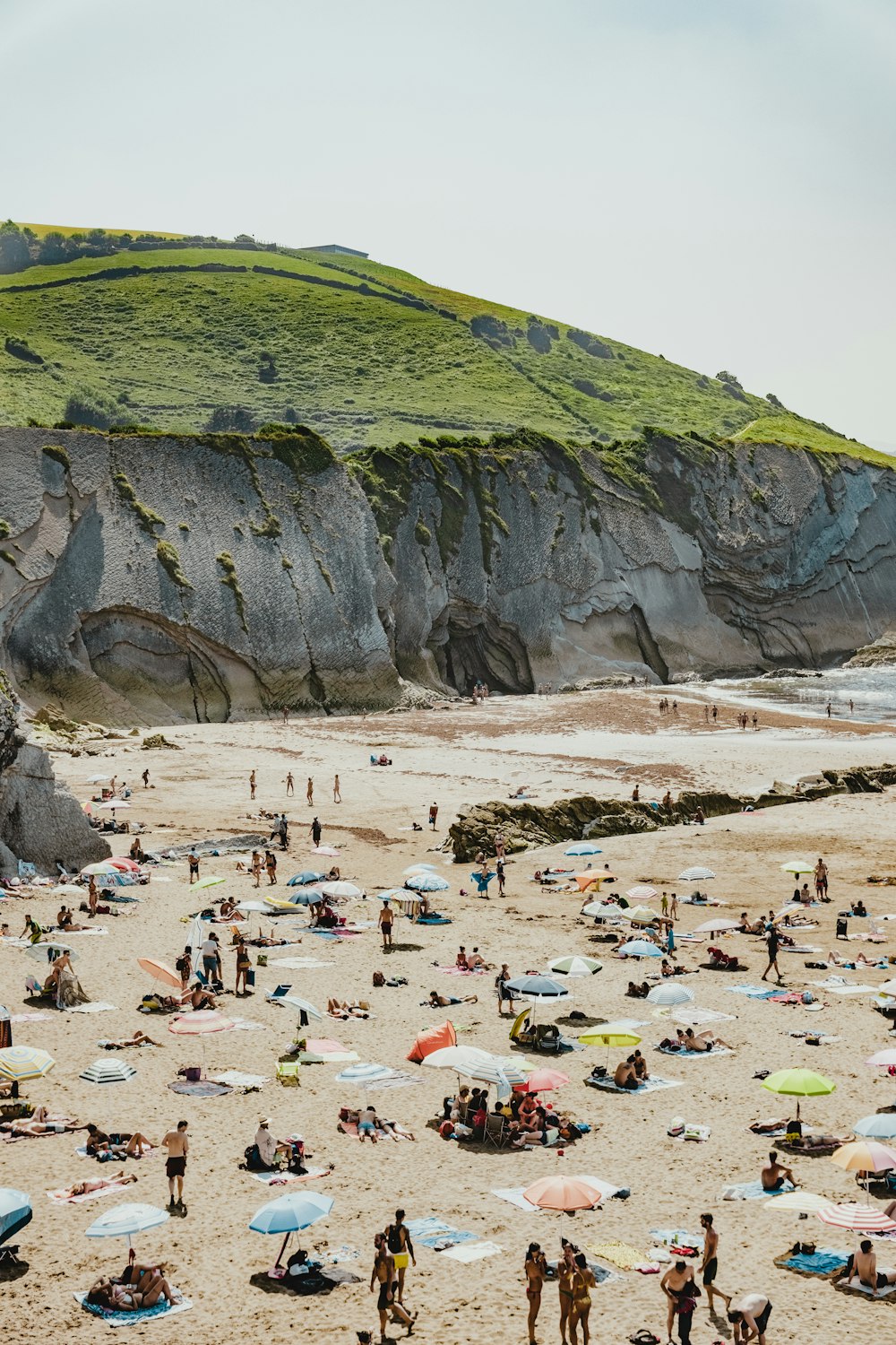 people on beach beside hill during daytime
