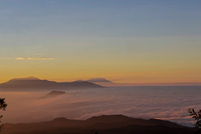 A serene mountain landscape at dawn with soft teal and deep blue hues blending into the sky.