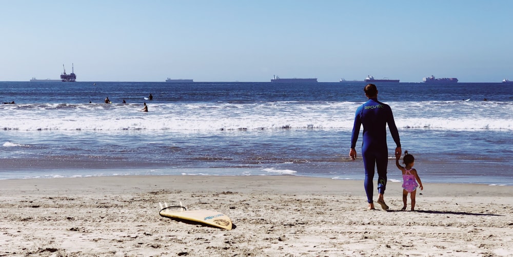 man holding girl while standing on beach