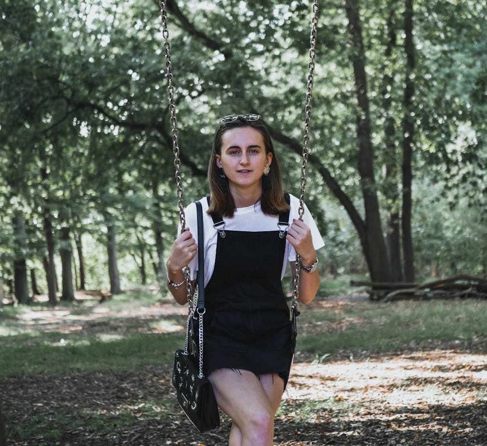 Femme assise sur une balançoire extérieure entourée de grands arbres verts