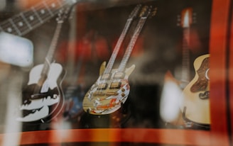 Multiple guitars are displayed behind glass in a shop, with reflections creating a layered effect. The instruments vary in design, highlighting their unique styles and craftsmanship.