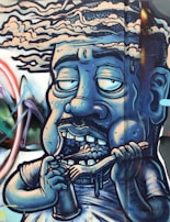 A graffiti-style artwork depicting a caricature of a human figure with a blue hue. The figure has exaggerated facial features, with half-closed, large eyes, a mustache, and showing teeth while holding a spoon and a cup. The background includes abstract shapes and vibrant colors, giving a dynamic feel to the mural.