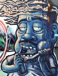 A graffiti-style artwork depicting a caricature of a human figure with a blue hue. The figure has exaggerated facial features, with half-closed, large eyes, a mustache, and showing teeth while holding a spoon and a cup. The background includes abstract shapes and vibrant colors, giving a dynamic feel to the mural.