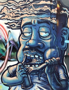 A graffiti-style artwork depicting a caricature of a human figure with a blue hue. The figure has exaggerated facial features, with half-closed, large eyes, a mustache, and showing teeth while holding a spoon and a cup. The background includes abstract shapes and vibrant colors, giving a dynamic feel to the mural.