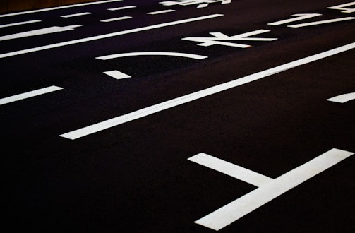 Dark asphalt road marked with white lane dividers and directional arrows, featuring clear Japanese kanji characters.