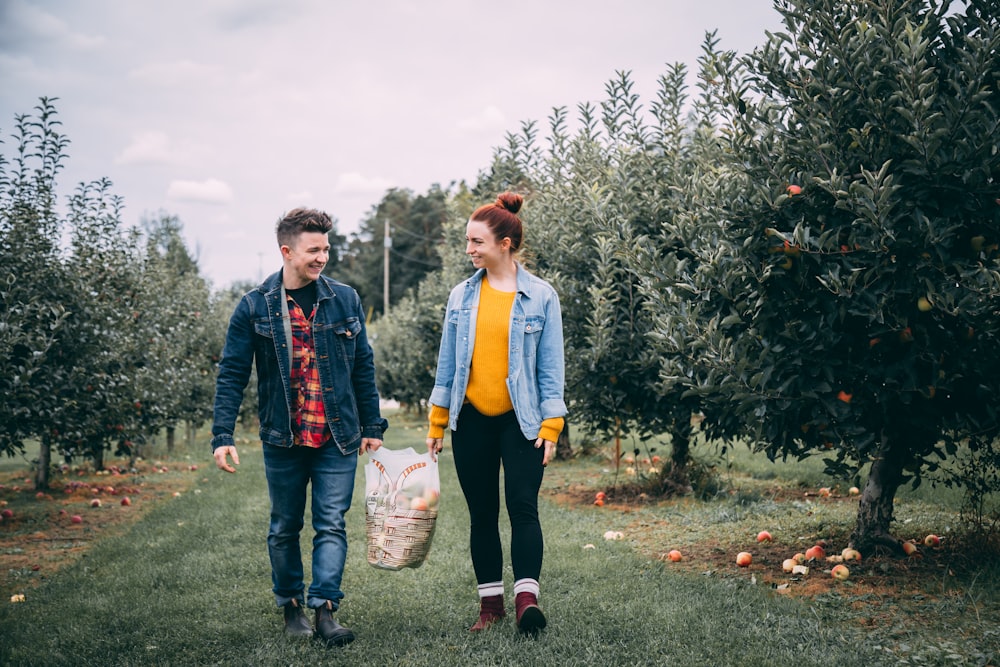 man carrying bag with woman in fruit tree orchard at daytime