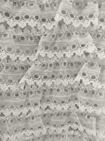Intricate white lace fabric with a delicate floral pattern and scalloped edges, layered in a cascading manner.