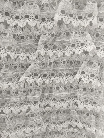 Intricate white lace fabric with a delicate floral pattern and scalloped edges, layered in a cascading manner.