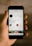 A hand is holding a smartphone displaying an Instagram profile. The profile belongs to a user named jakobowens, featuring a circular profile picture, user stats, and several icons for various Instagram functions. The screen shows text denoting the number of posts, followers, and following, along with buttons for promoting and editing the profile. Below the profile information are icons for IGTV, highlights, and YouTube, among others. The background is blurred, focusing attention on the phone and its screen.