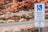 A parking sign designating handicapped parking with a minimum fine for violation. The sign also indicates that the space is van accessible. It is set against a background of red rocky terrain and roadside vegetation.